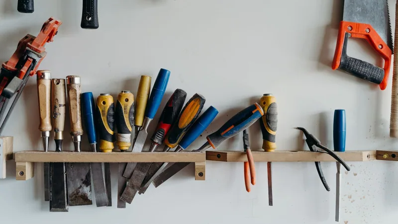 Chisels, screwdrivers and a saw hung on a wooden rack against a white workshop wall